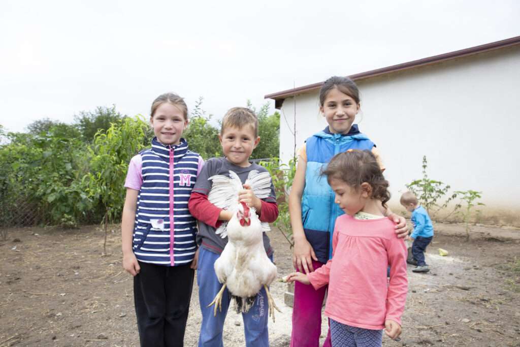 Moldovan children holding chicken outside of home